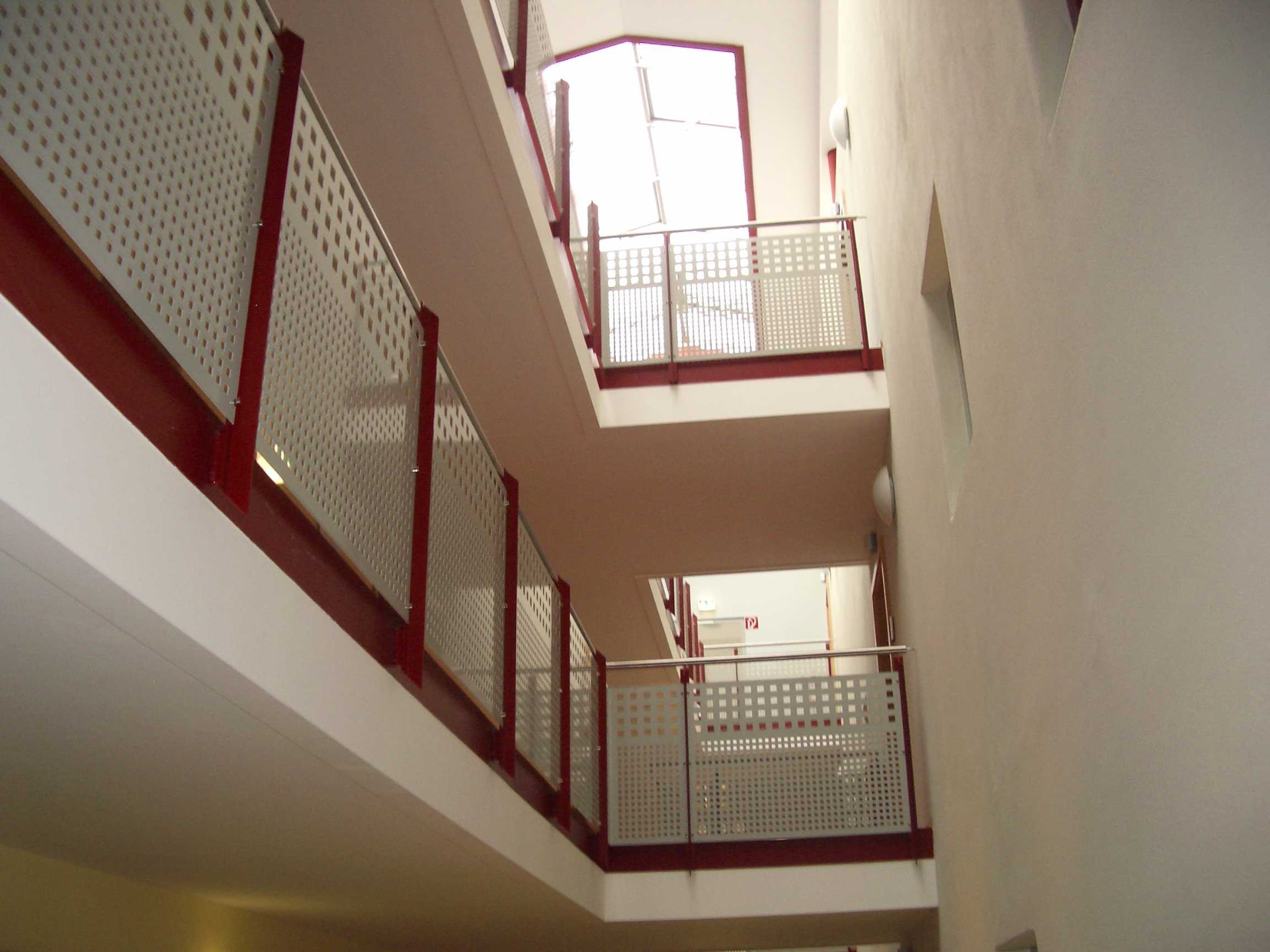 Weißes Treppenhaus mit gelochten Metallgeländern
