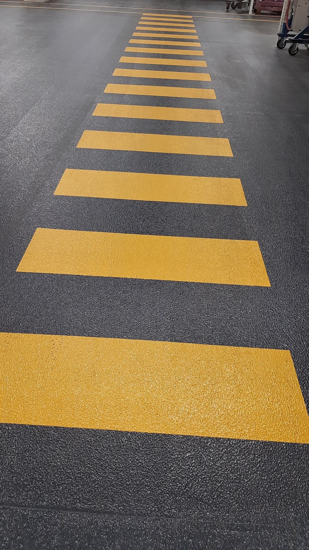Gelbe Zebrastreifen-Markierung auf dunklem Hallenboden